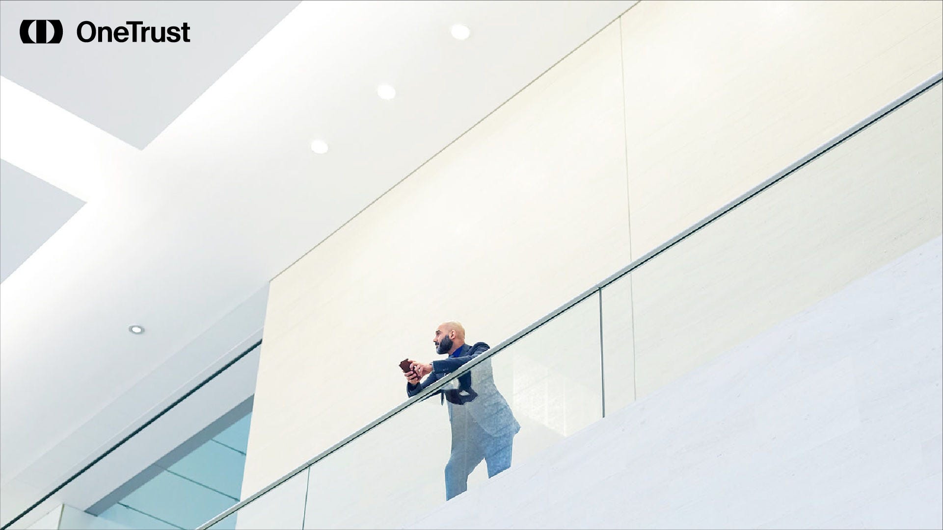 Person standing on a modern office balcony using a mobile device, with the OneTrust logo visible, representing digital governance and AI compliance planning.